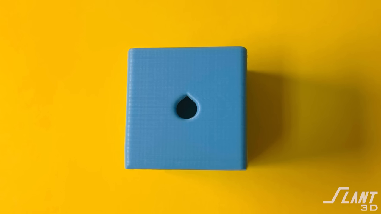 Close-up of a 3D printed blue cube featuring a teardrop-shaped side hole to prevent sagging.
